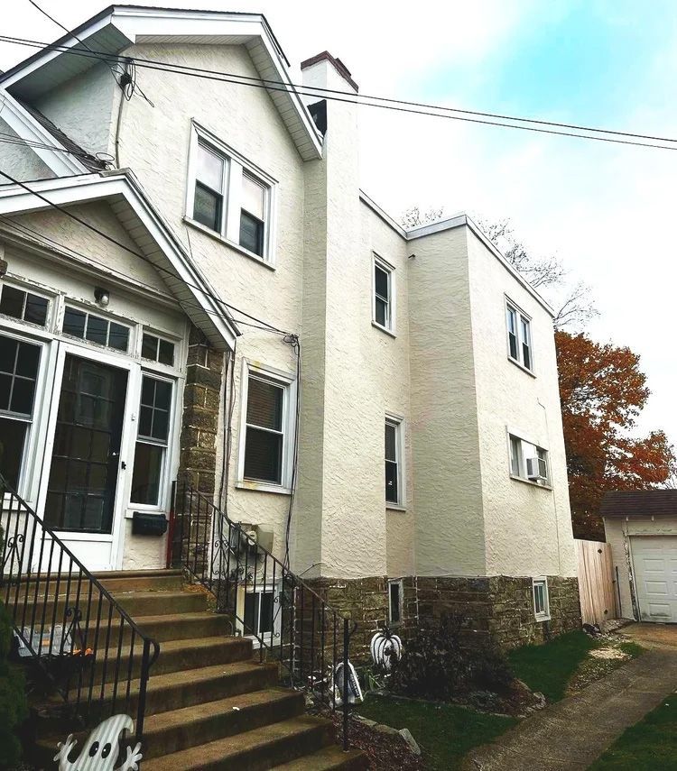 Multi-story house with stone foundation, stucco siding, and steps leading to front door.