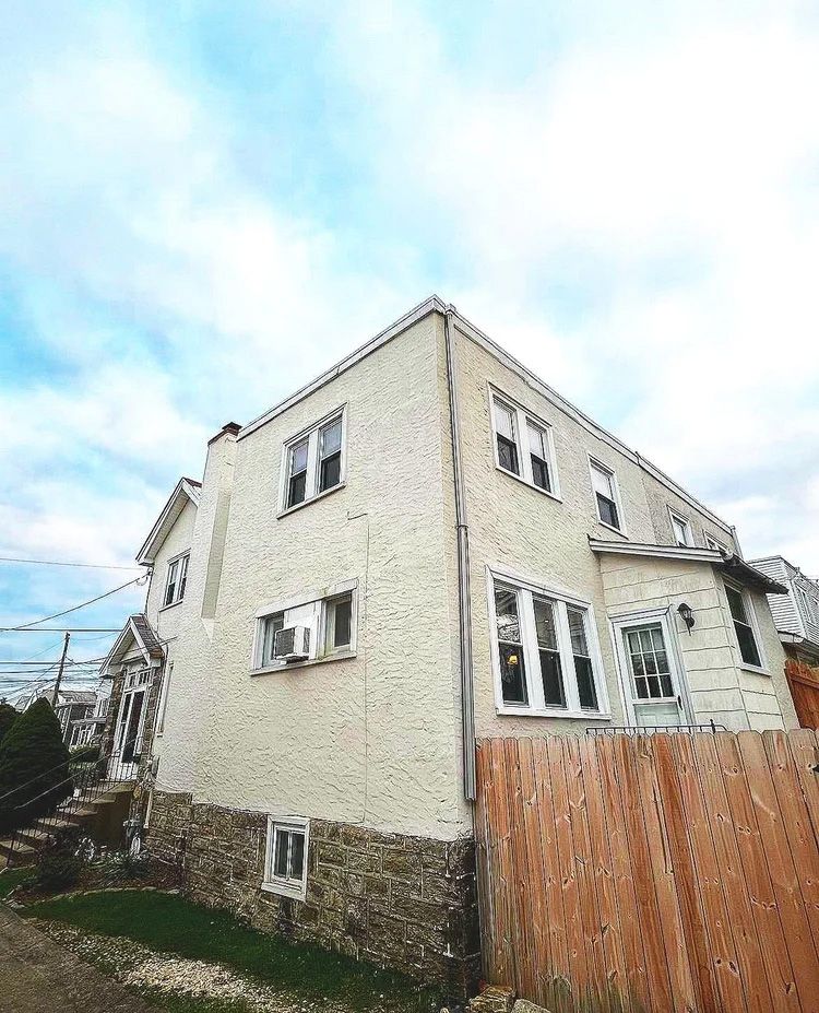 Two-story house with stucco exterior and wooden fence. Cloudy sky.