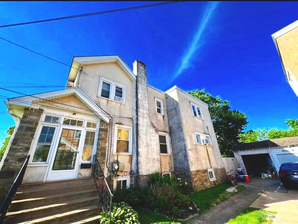 Two-story house with stone facade, chimney, and porch under a blue sky.