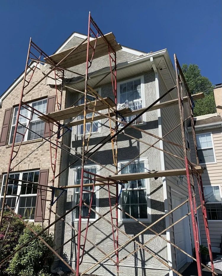 House exterior with scaffolding. Siding repair underway on a two-story building on a sunny day.
