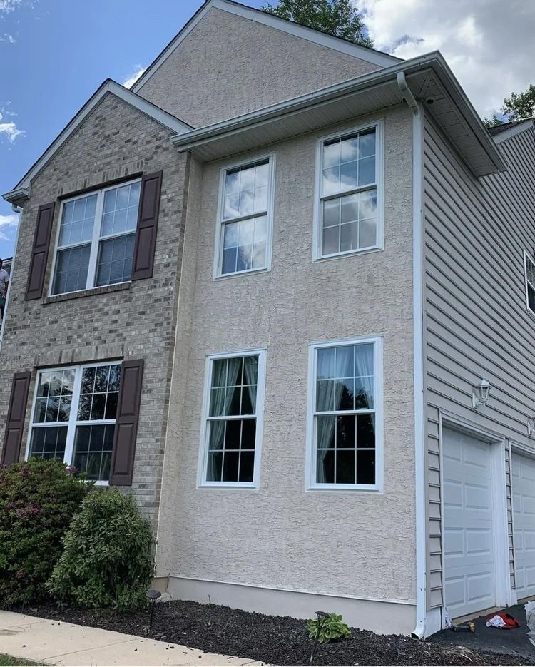 Two-story house with brick and stucco siding, white windows, and a garage on a sunny day.