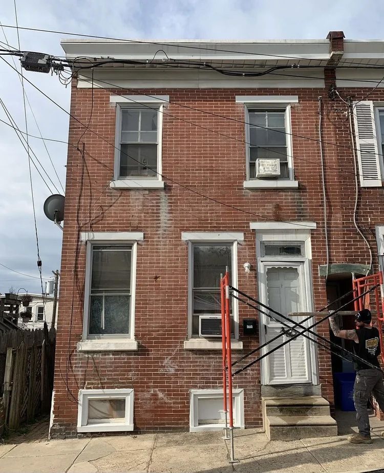 Brick row house with two stories. Scaffolding, electrical wires, and windows present.