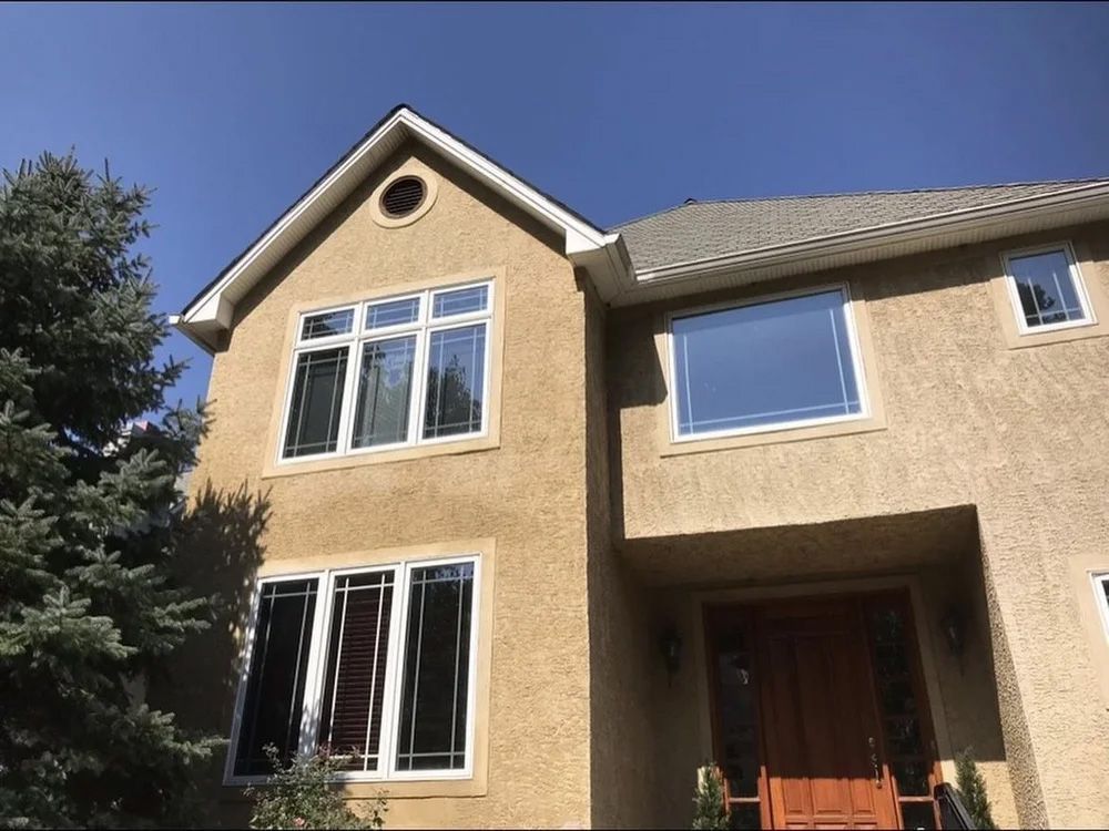 Two-story beige house with white trim windows and a brown door under a blue sky.