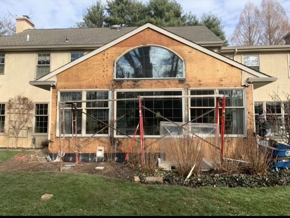 Rear of house under construction with scaffolding, exposed wood, and large windows.