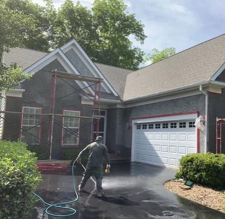 Man power washing a house with scaffolding and dark driveway.