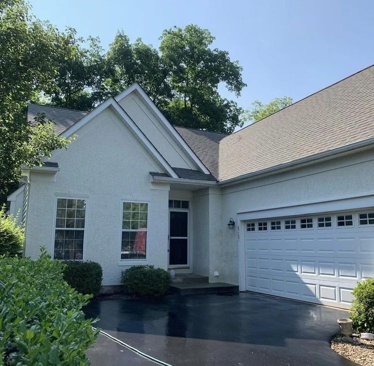 White stucco house with dark roof, two windows, black driveway, and attached garage.