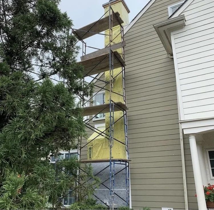Scaffolding next to a house's chimney; house is being worked on.