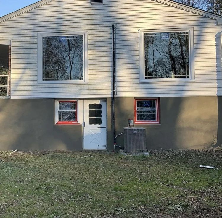 Back of a house with white siding, large windows, and a gray concrete foundation.