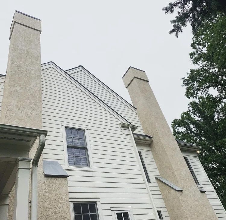 Exterior view of a white house with two tall chimneys against a cloudy sky.