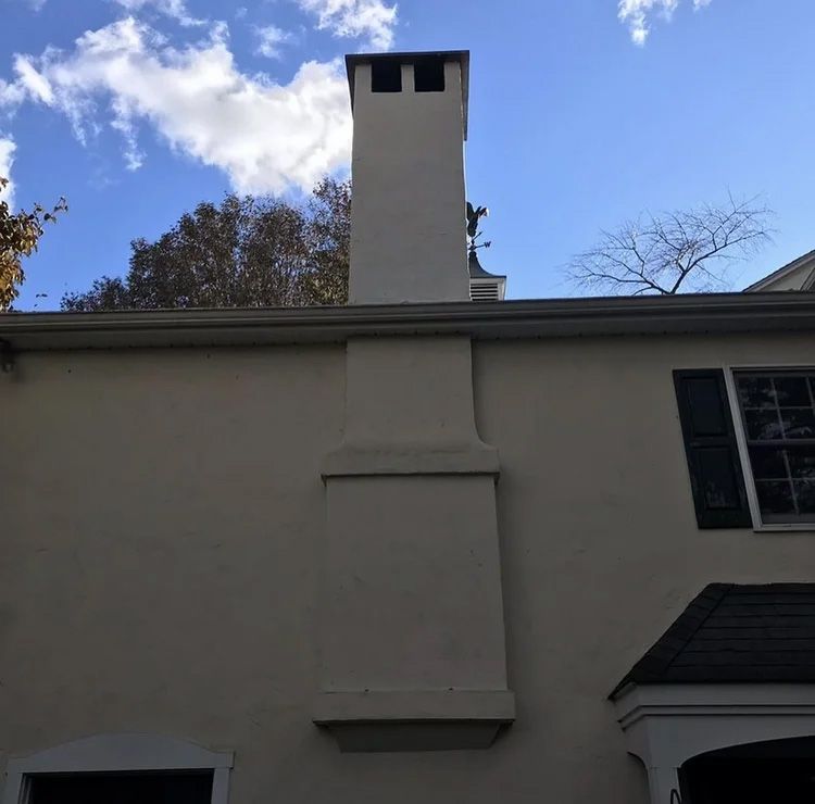 Tall chimney on a cream-colored building. Blue sky, some clouds, and trees in the background.