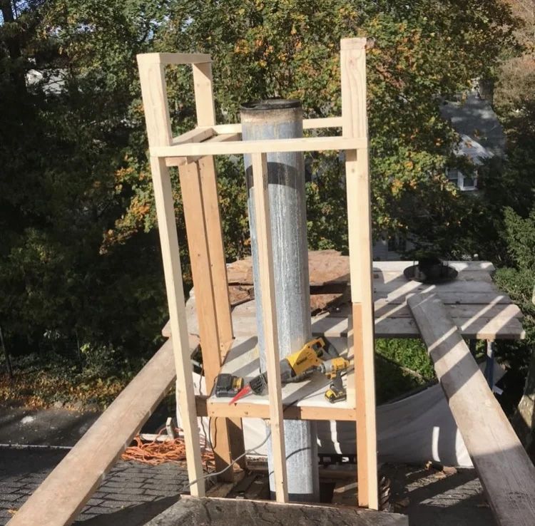 Wooden scaffolding supports a chimney on a rooftop; a drill and tools rest on the structure.