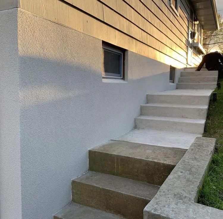 Concrete steps leading up to a building with a window, grassy area to the right, and person at top.
