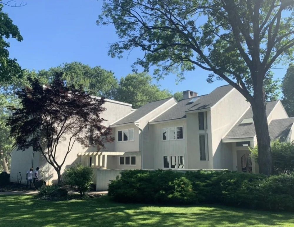 Cream-colored house with multiple levels, trees, and green bushes on a sunny day.