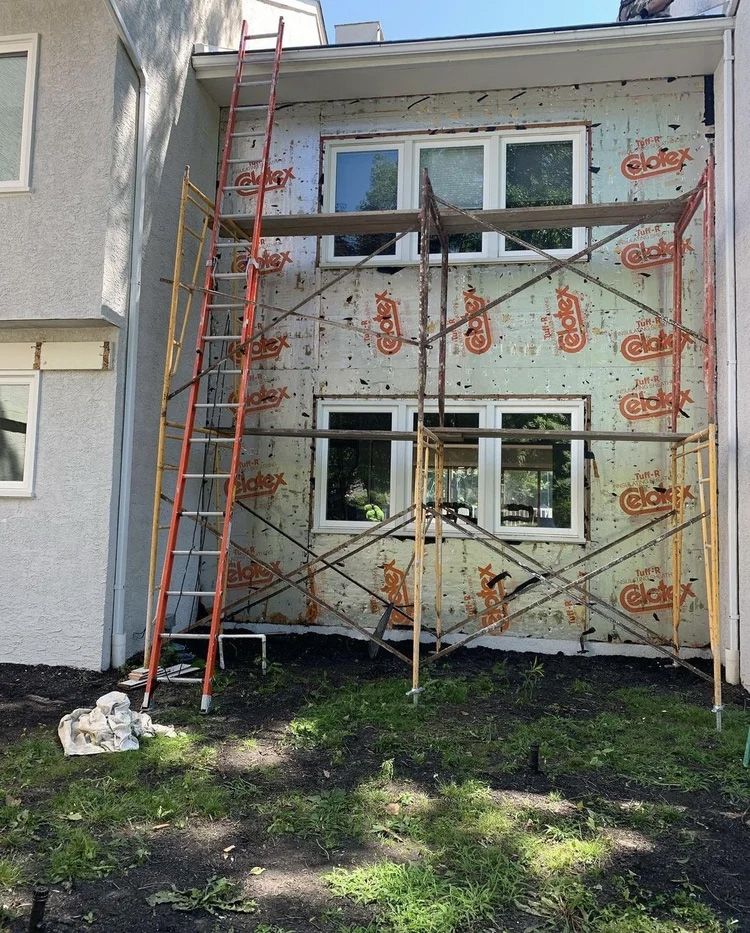 Building exterior under renovation; scaffolding and ladder present. Insulation visible around windows.