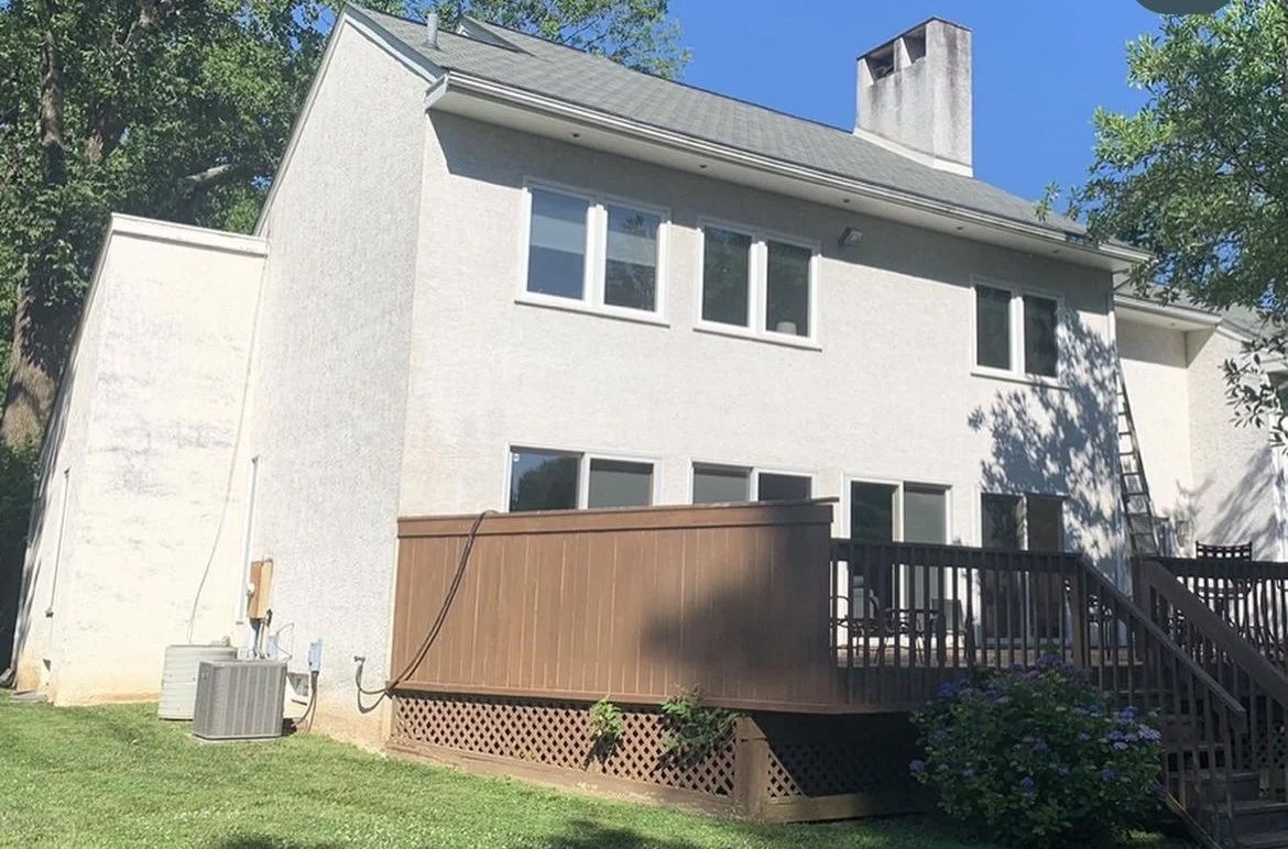 Back view of a two-story white house with a brown wooden deck, set on green grass.