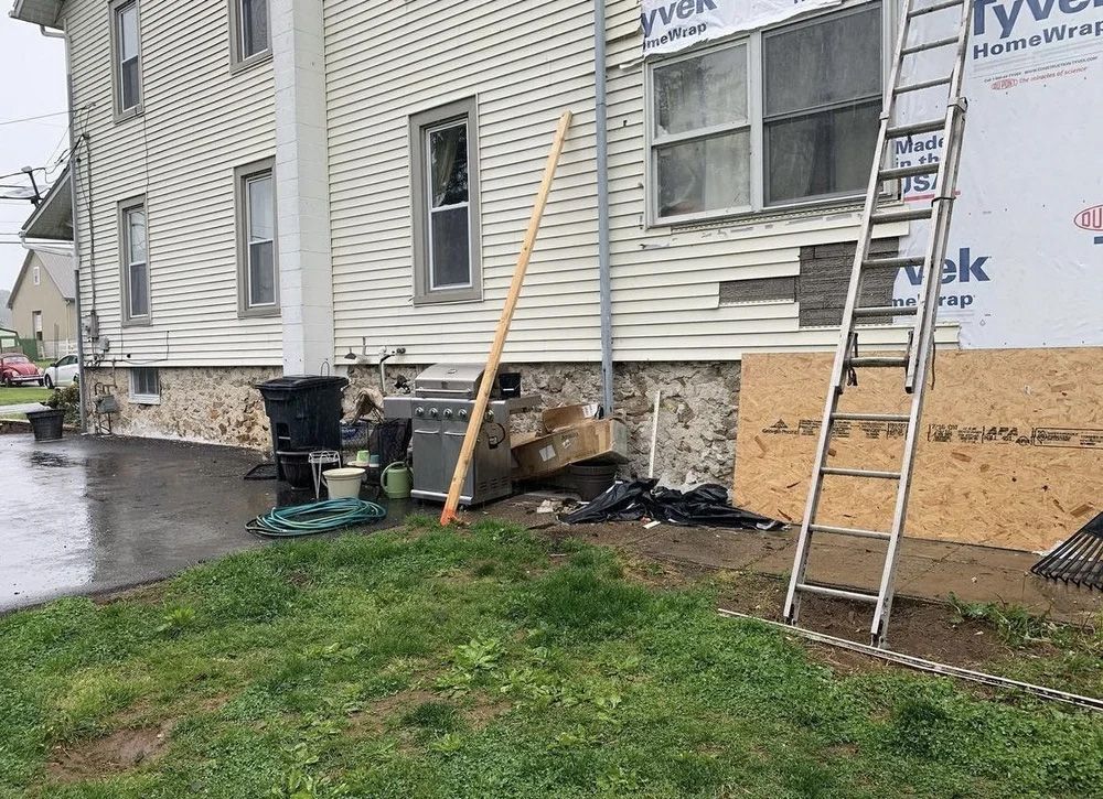 Exterior of a building under renovation with exposed wall, ladder, and debris on the ground.