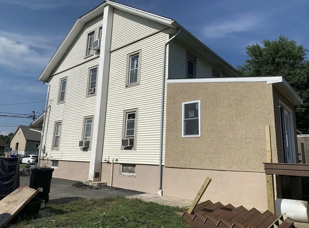 Side view of a two-story house with tan siding and a stucco addition.