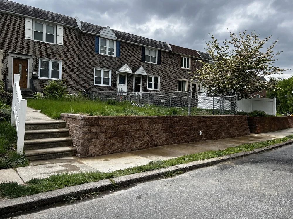 Row of brick townhouses with a retaining wall and stairs leading up to a grassy yard.
