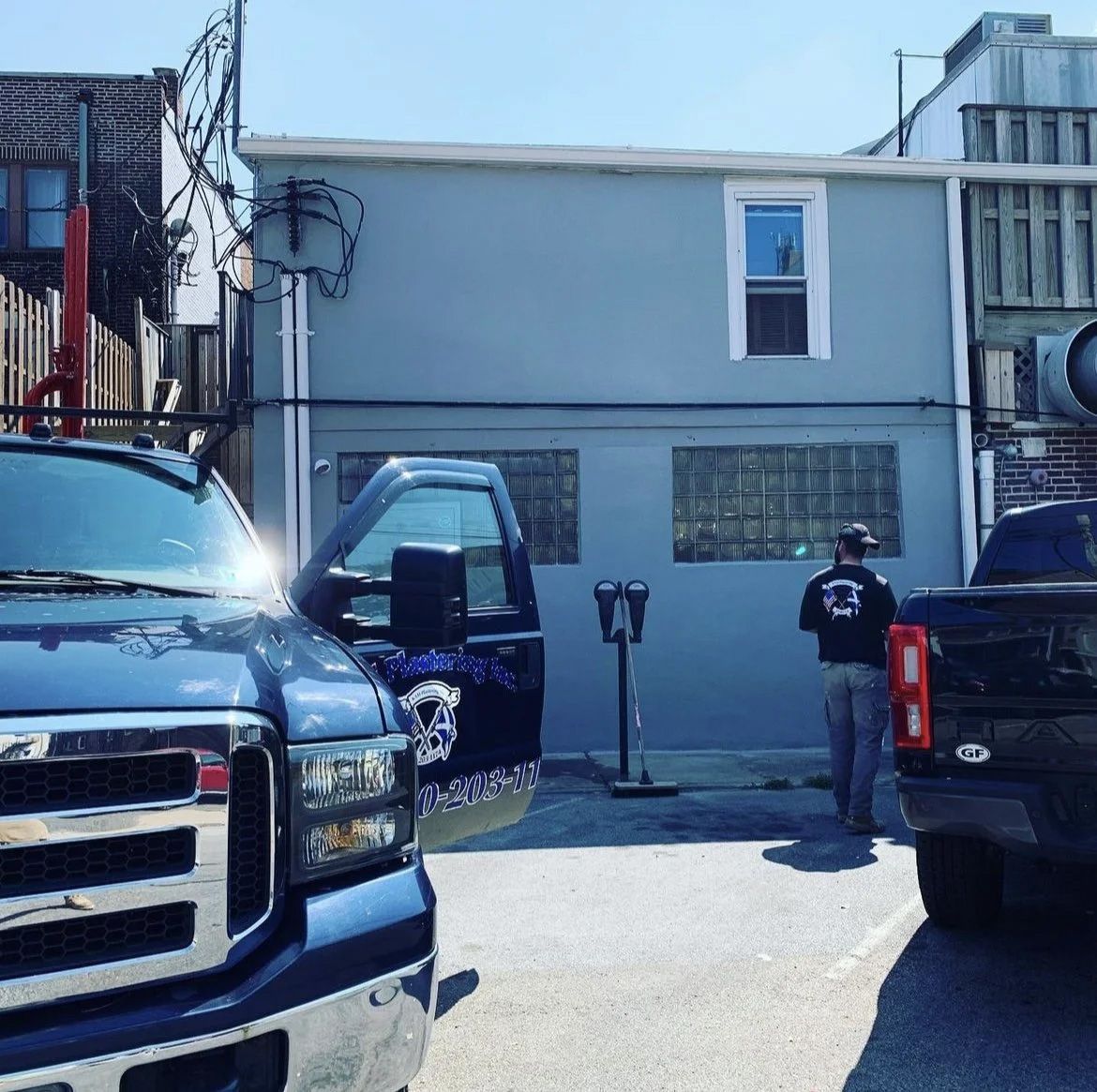 Blue trucks parked near a light blue building, with a person standing by a door.