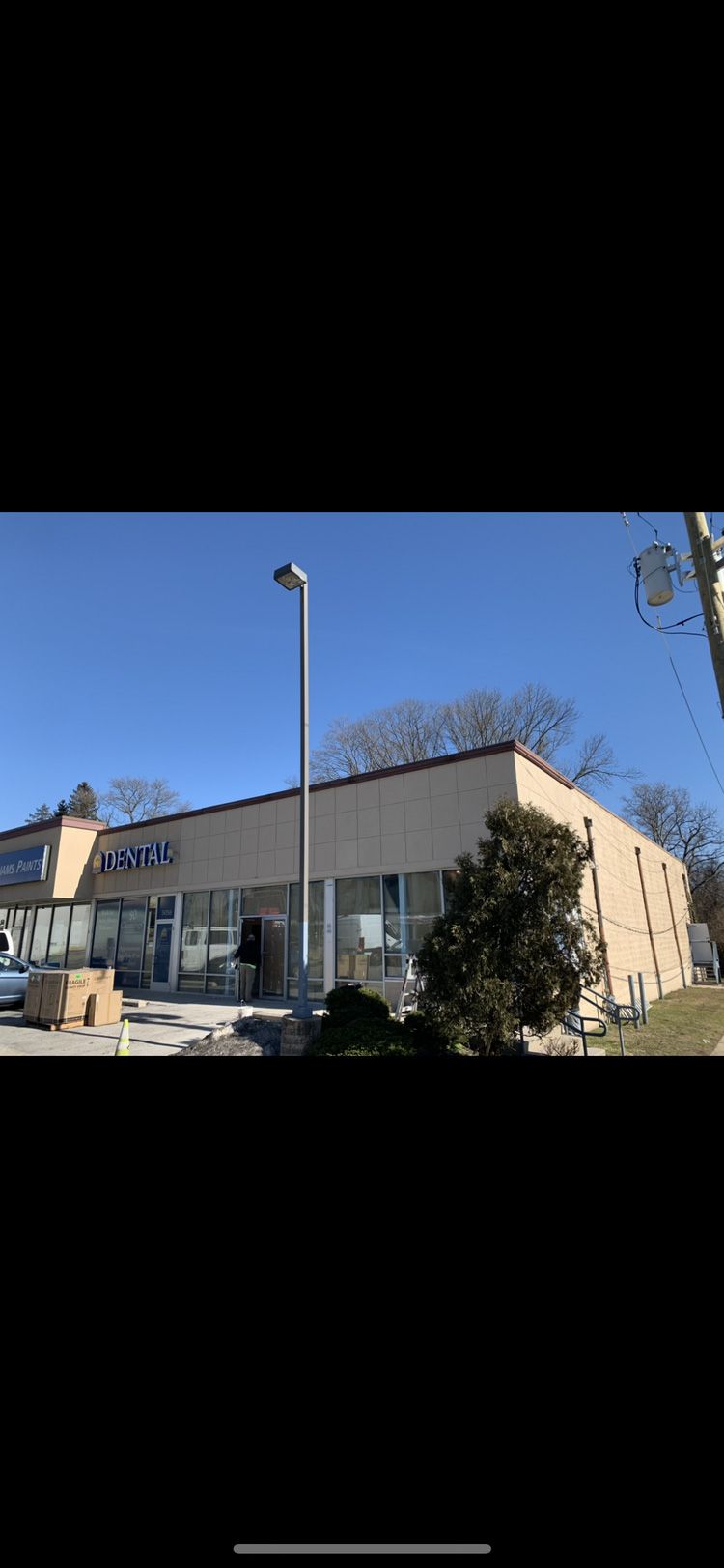 Exterior of a light-colored commercial building with large windows, a sign, a tree, and a clear blue sky.