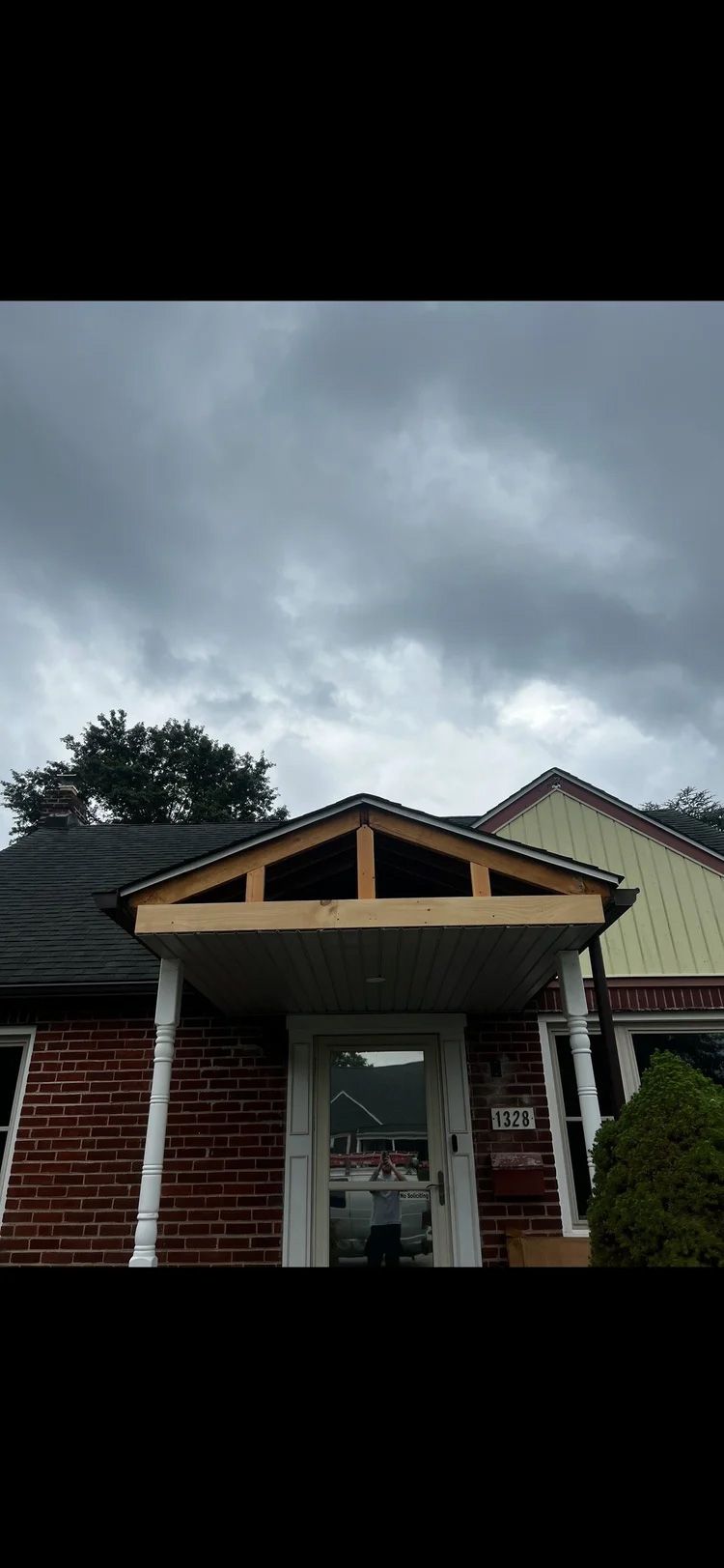House porch with unfinished wooden framework under a cloudy sky.