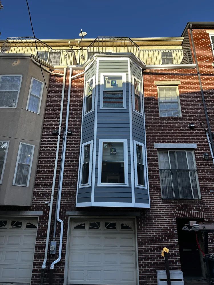 A multi-story brick building with a new gray bay window and white trim.