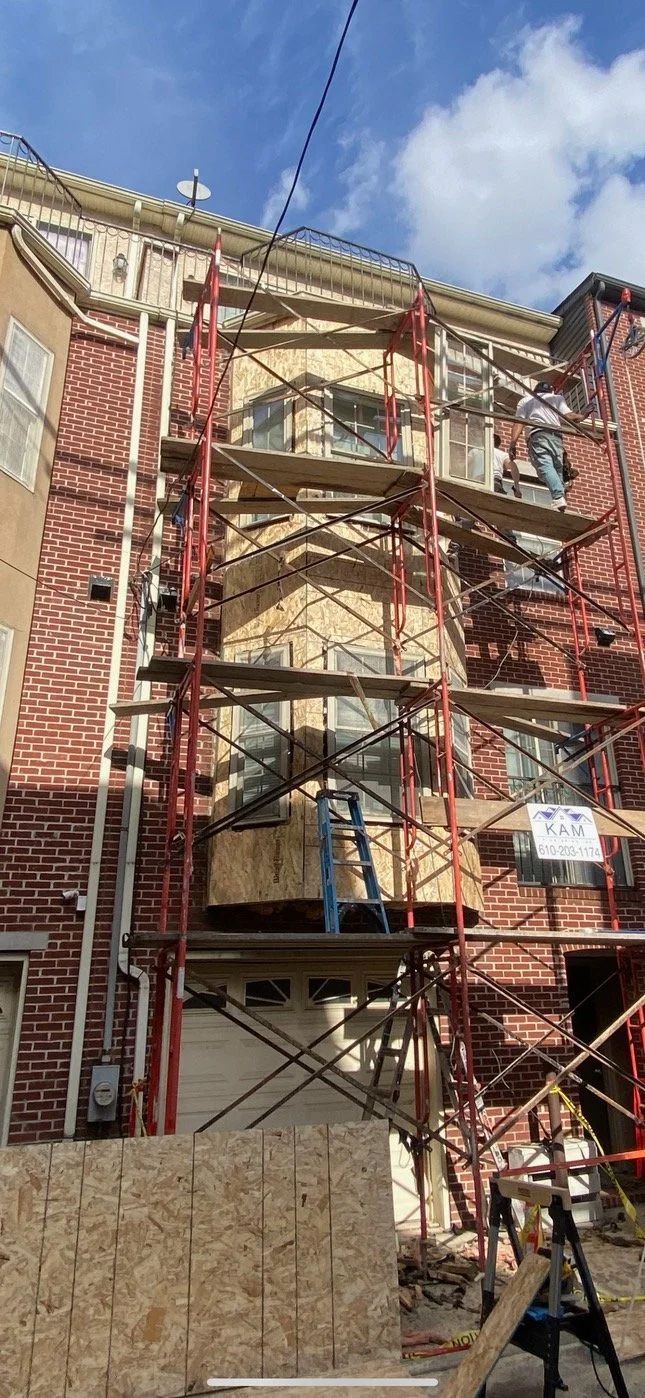 Building exterior under construction; scaffolding, brick, wood, and blue sky.