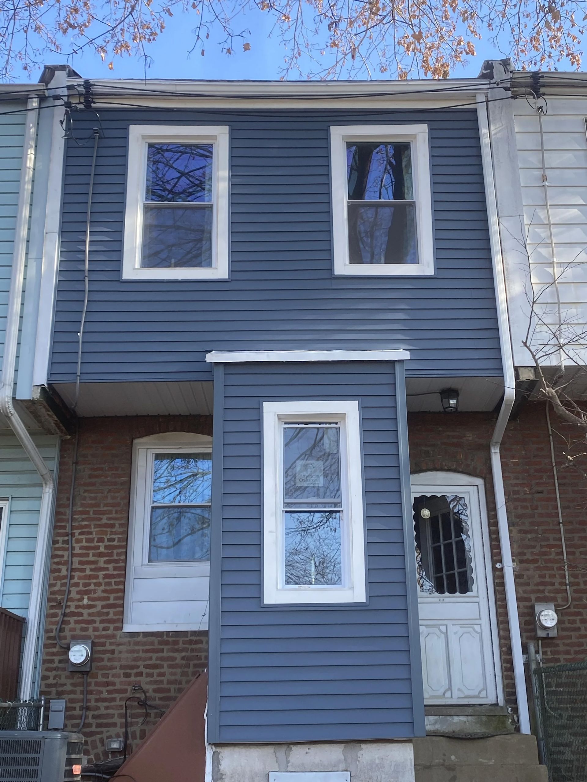 Blue clapboard-sided building facade with three windows. Brick base. White trim. Blue siding.