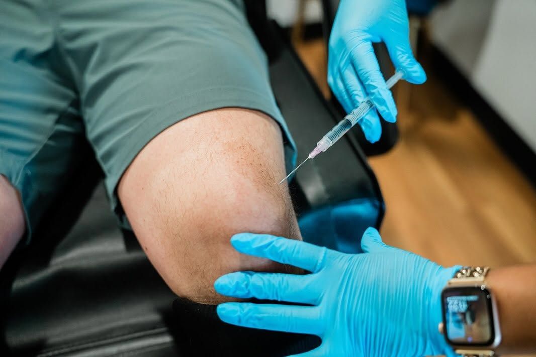 Gloved clinician gives an injection into a patient’s upper arm in a medical setting
