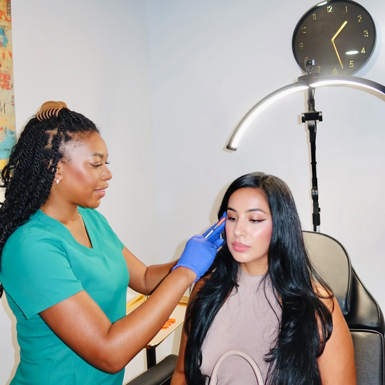 Two women in a salon, one applying makeup to the other's face under a ring light.