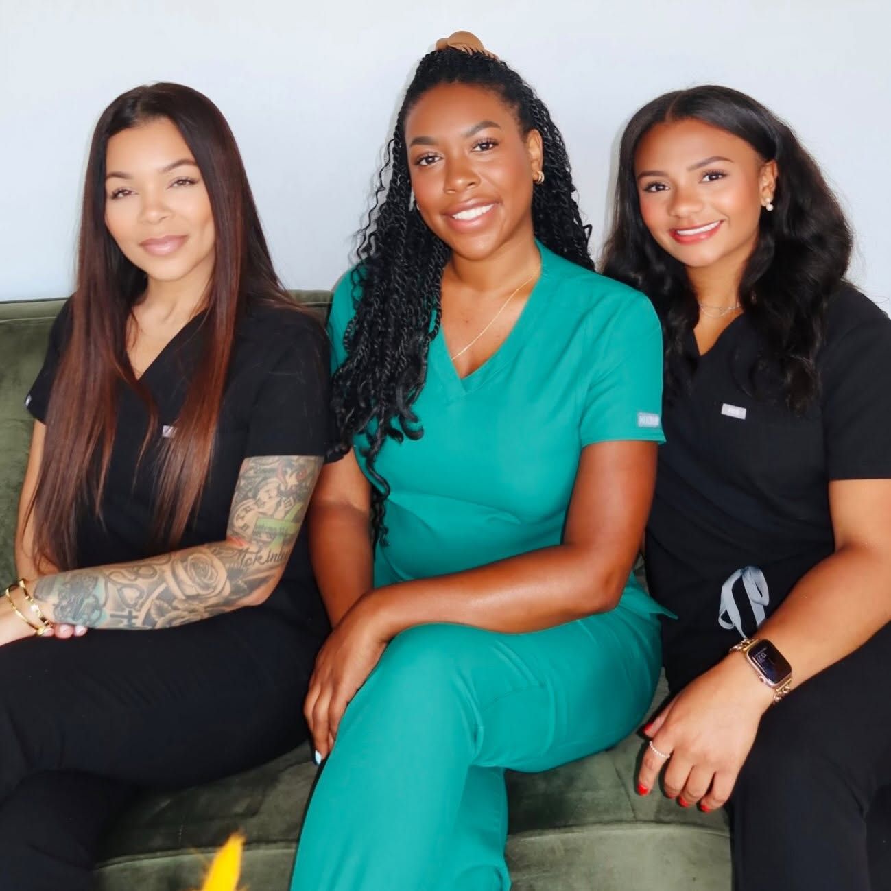 Three women seated together, smiling at the camera, wearing black and teal outfits.