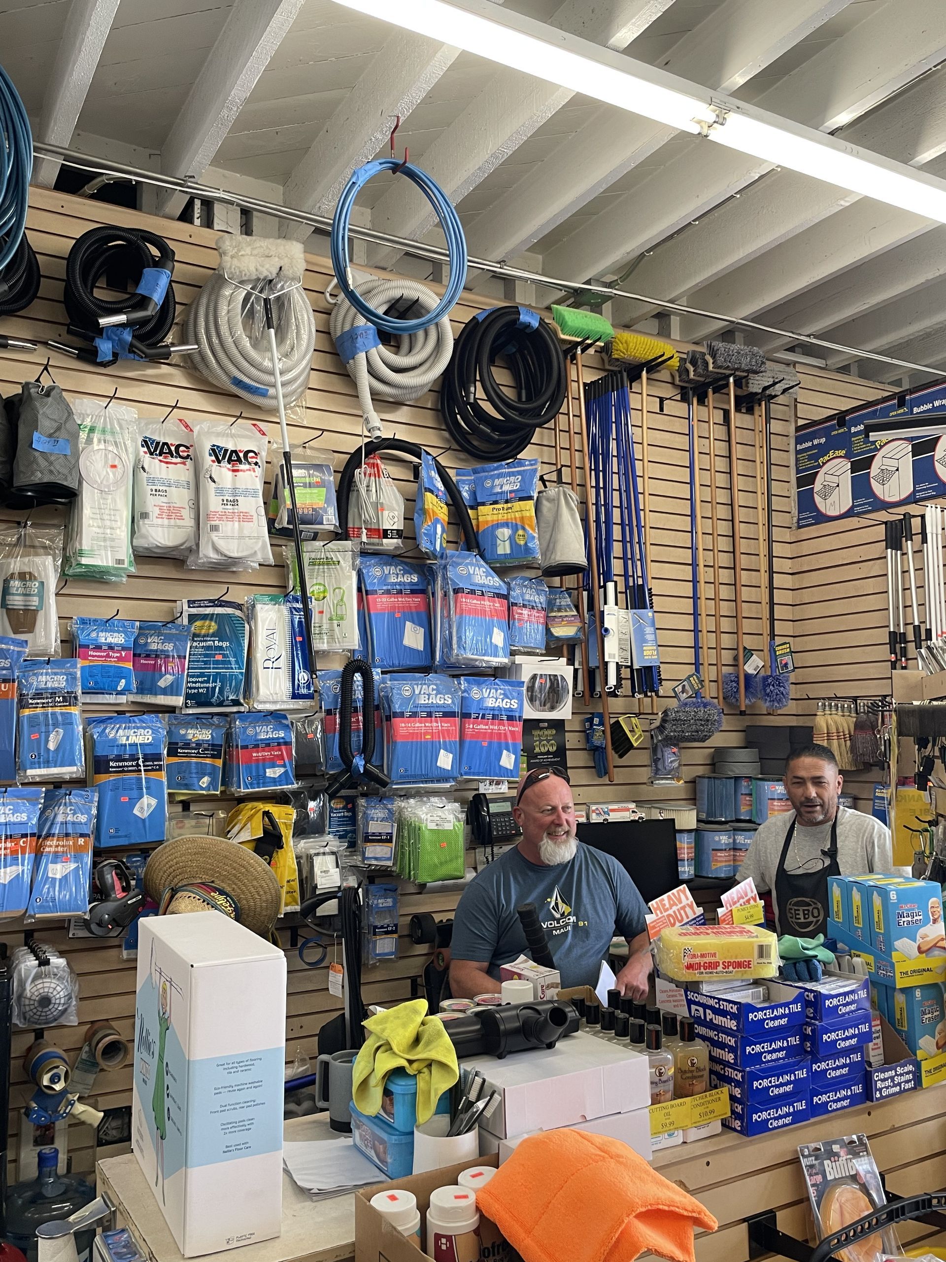 Two men at a shop counter in a hardware store, merchandise displayed on walls.