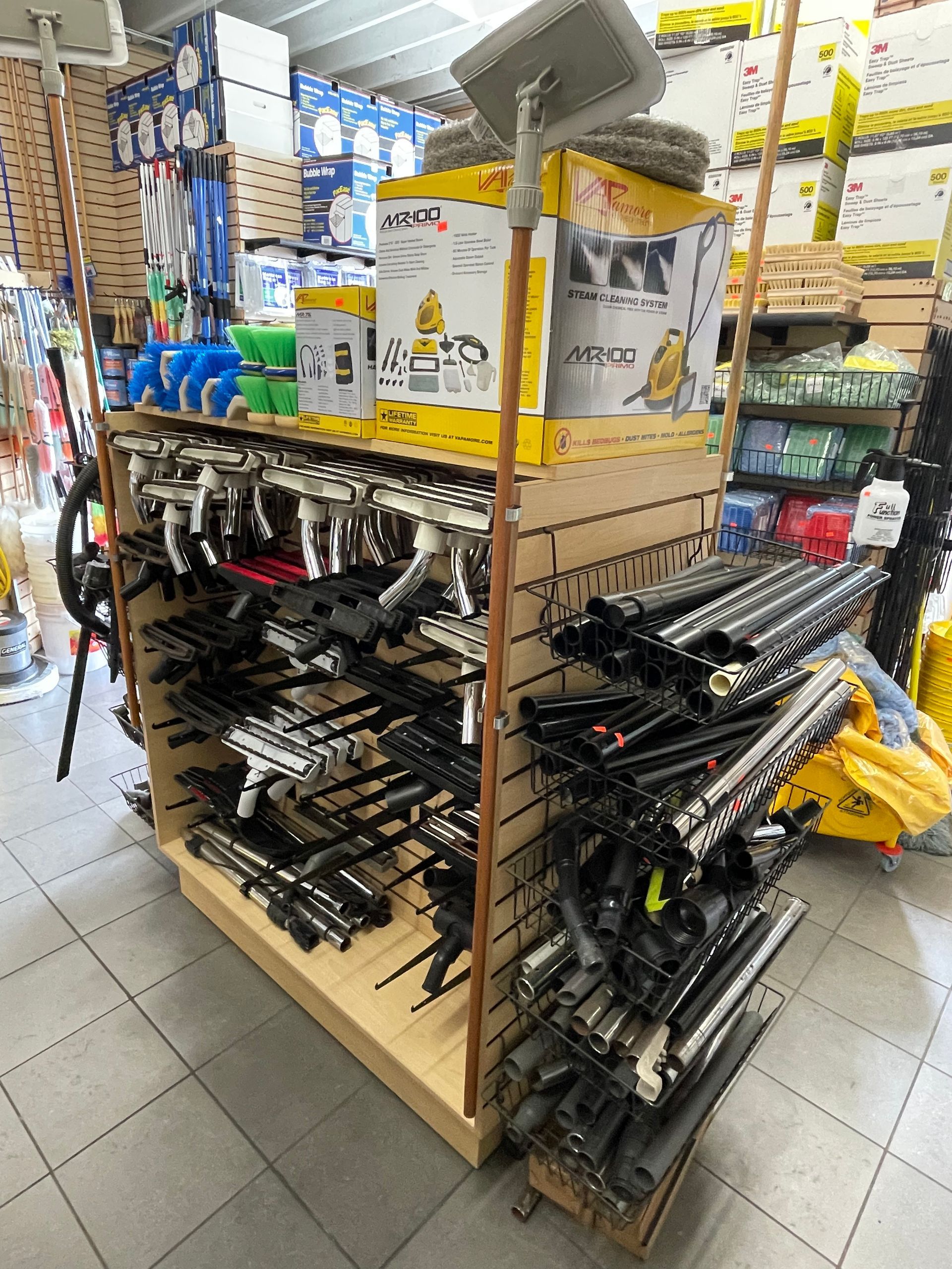 Display rack of spray guns and accessories in a hardware store with a yellow banner and copper pipes.