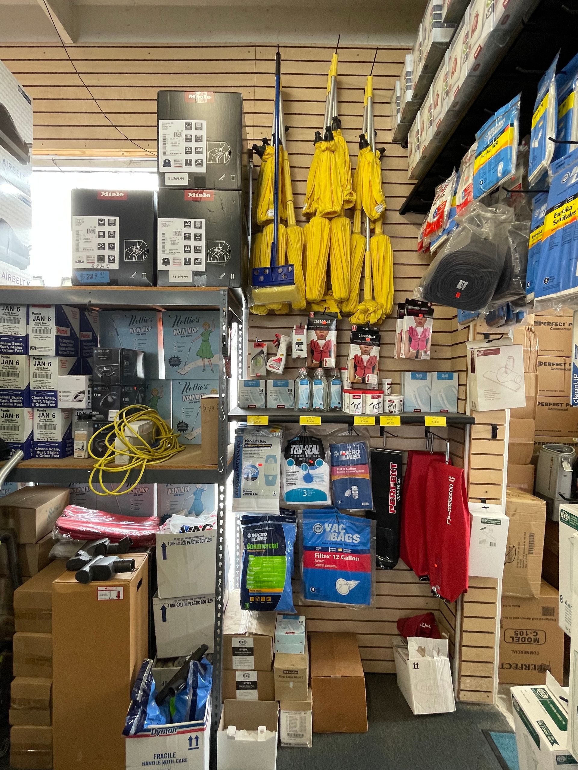 Shelf in a hardware store displaying mops, boxes, and various tools, mostly in shades of blue, yellow, and brown.