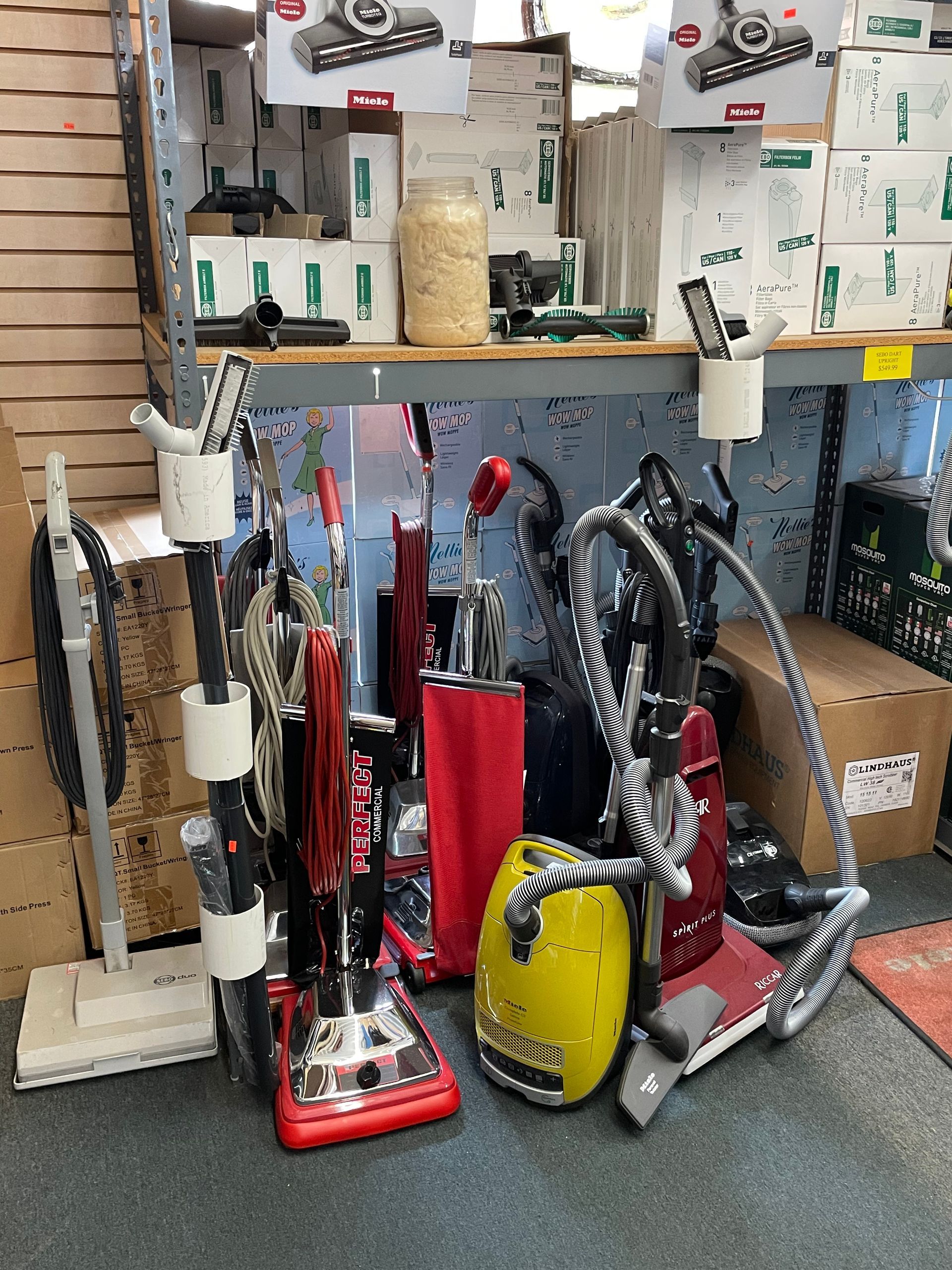 Vacuum cleaners displayed in a store. Red, black, and yellow upright models are in a row.