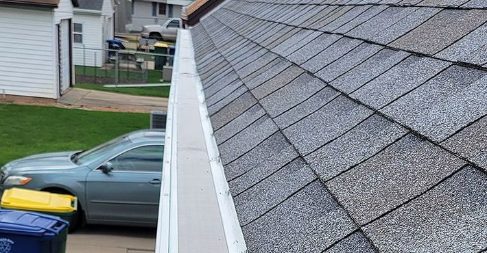A car is parked in a driveway next to a gutter on a roof