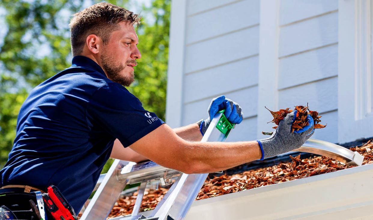 A man is cleaning gutters on the roof of a house