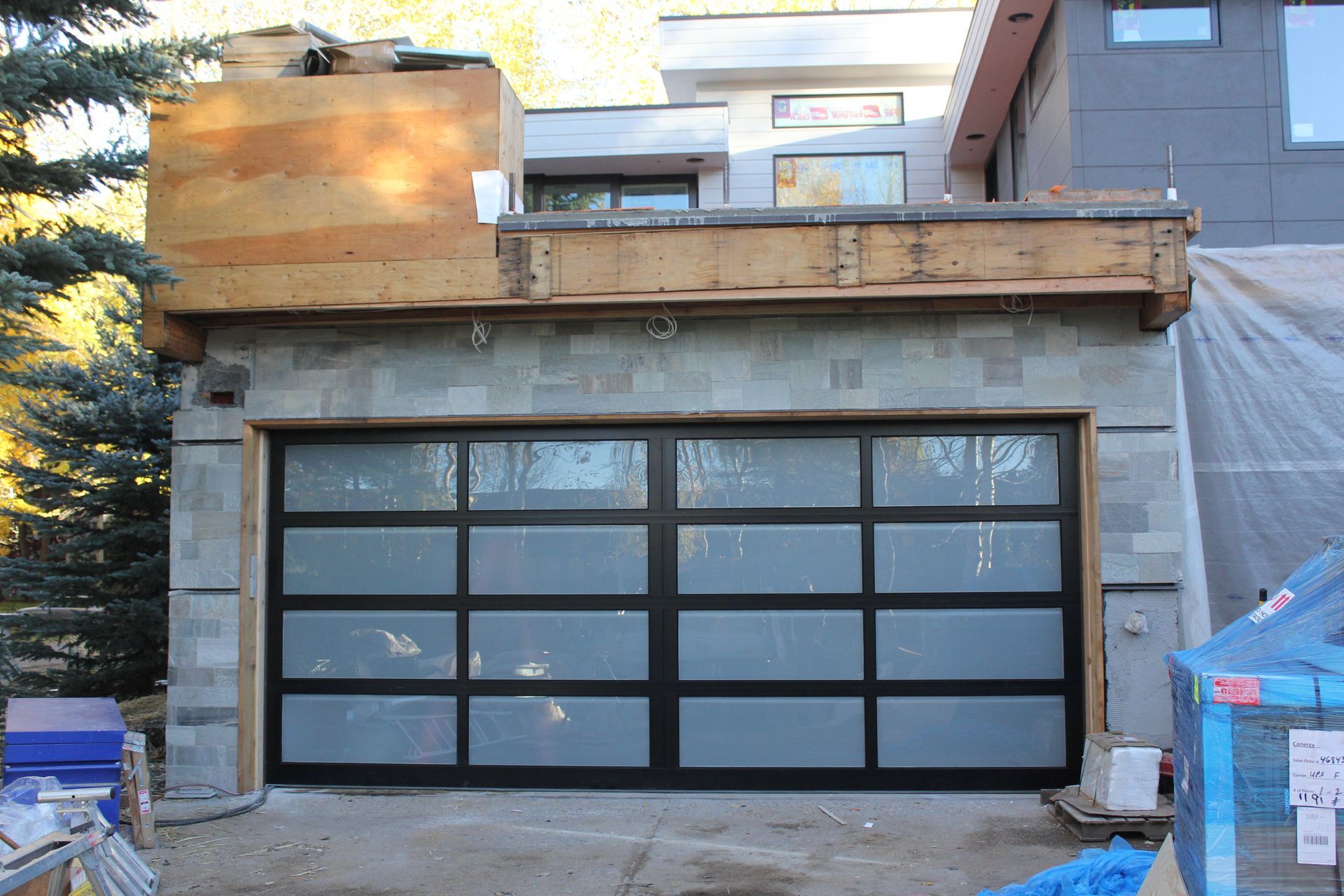 Garage with glass door under construction; gray block walls, wooden structure above.