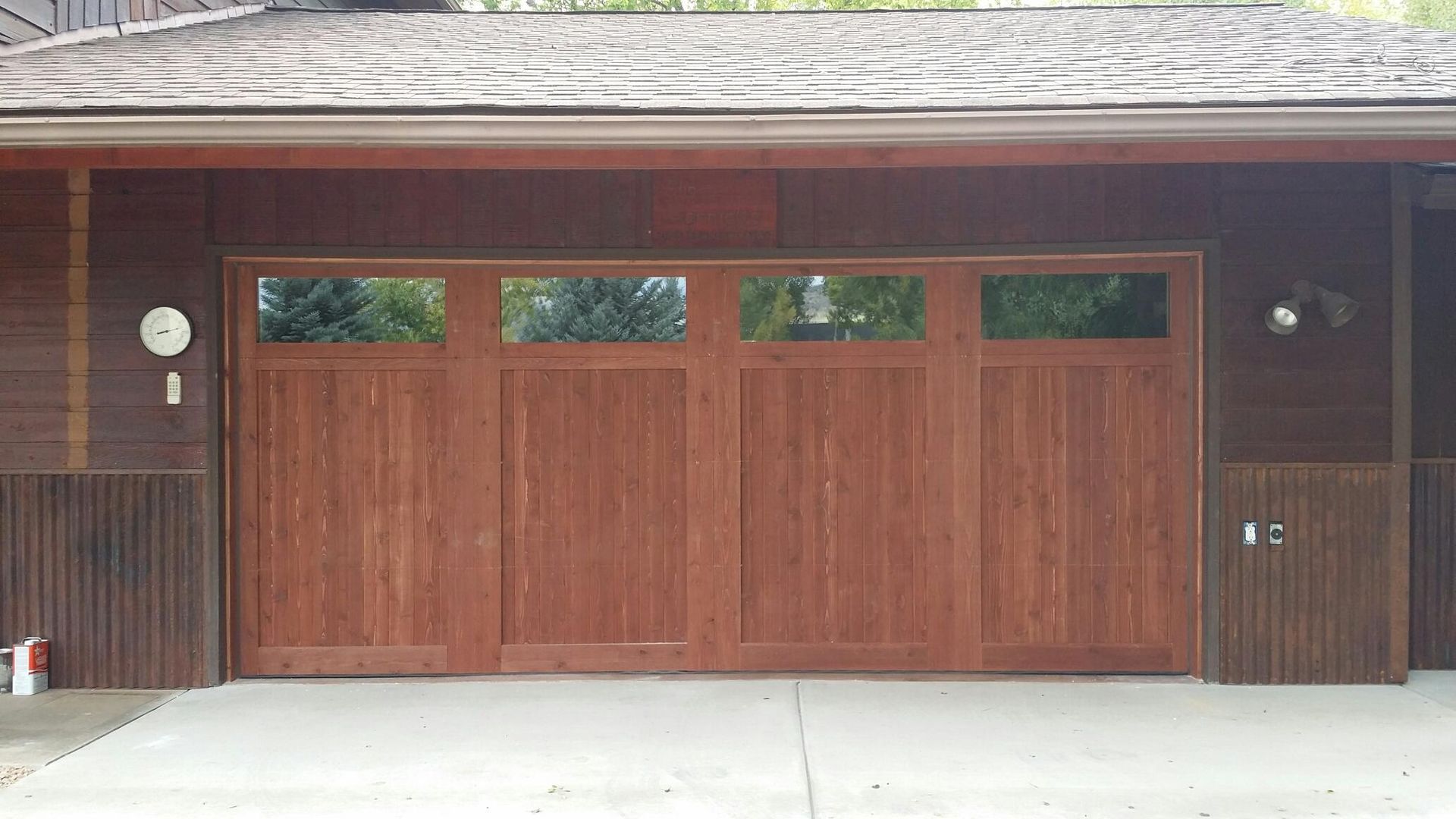 Wooden garage door with windows above, set in a brown building with a concrete driveway.