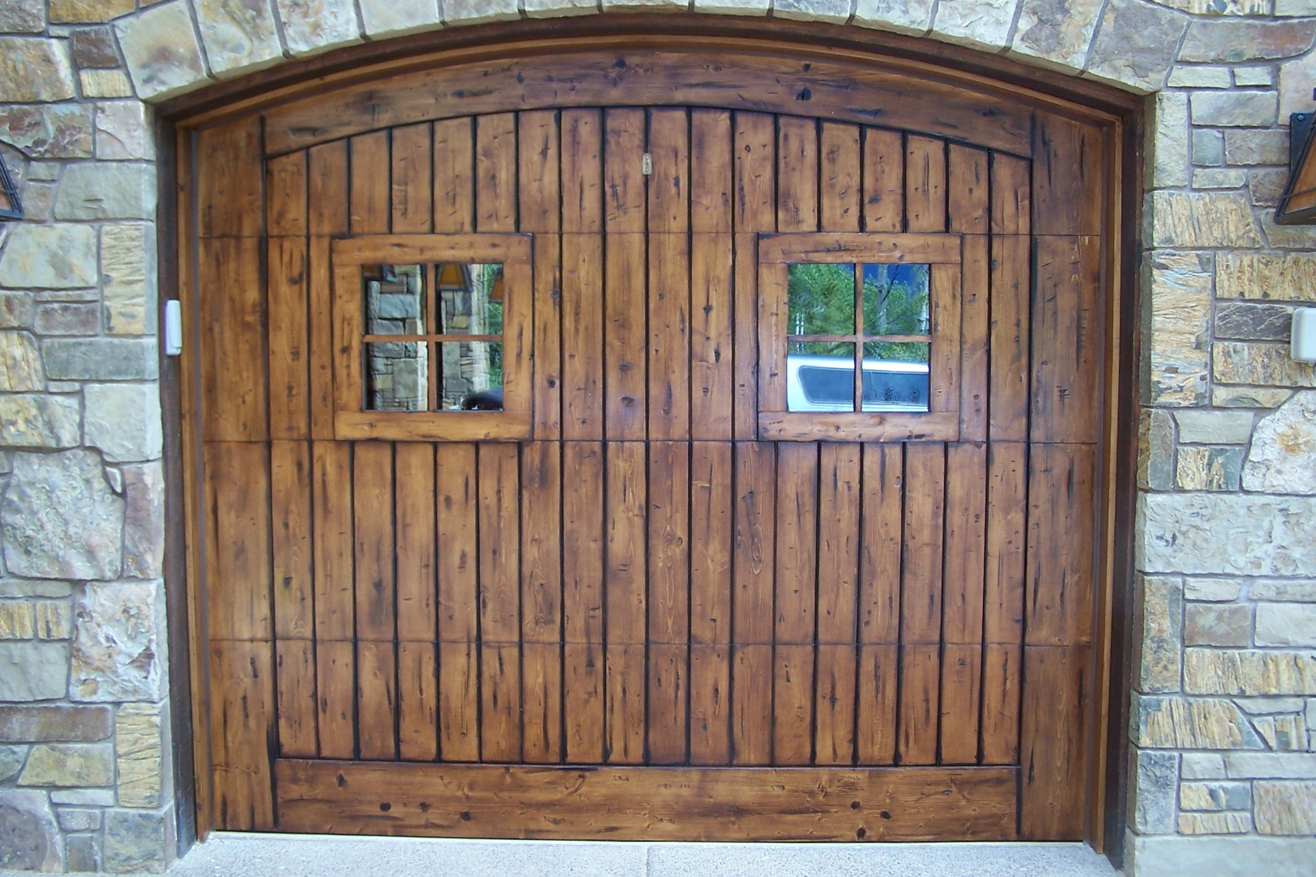 Wooden garage door with two small square windows, set in a stone archway.