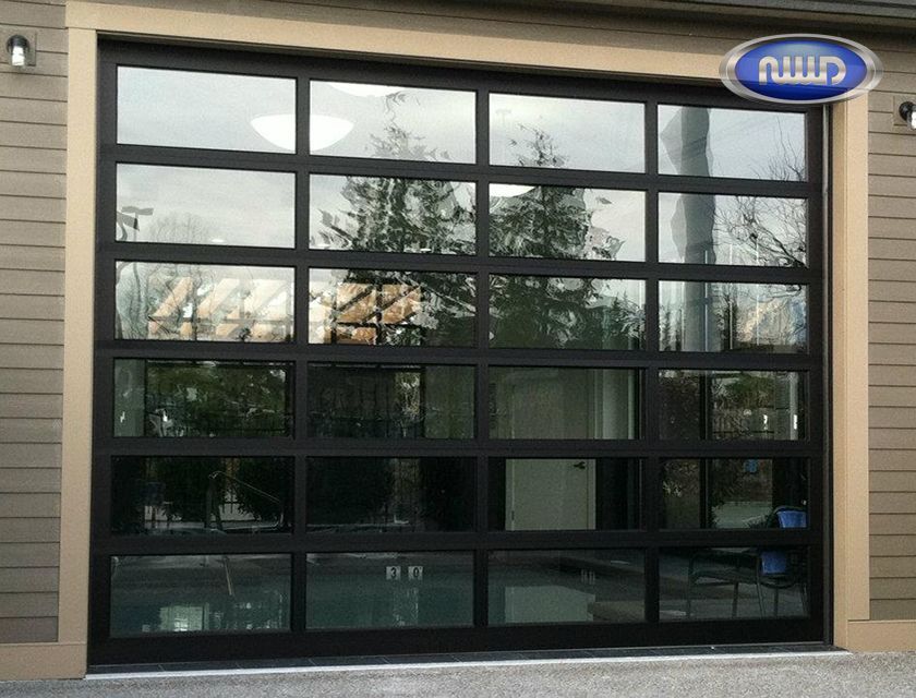 Black-framed glass garage door reflecting trees and sky; installed in a beige building exterior.