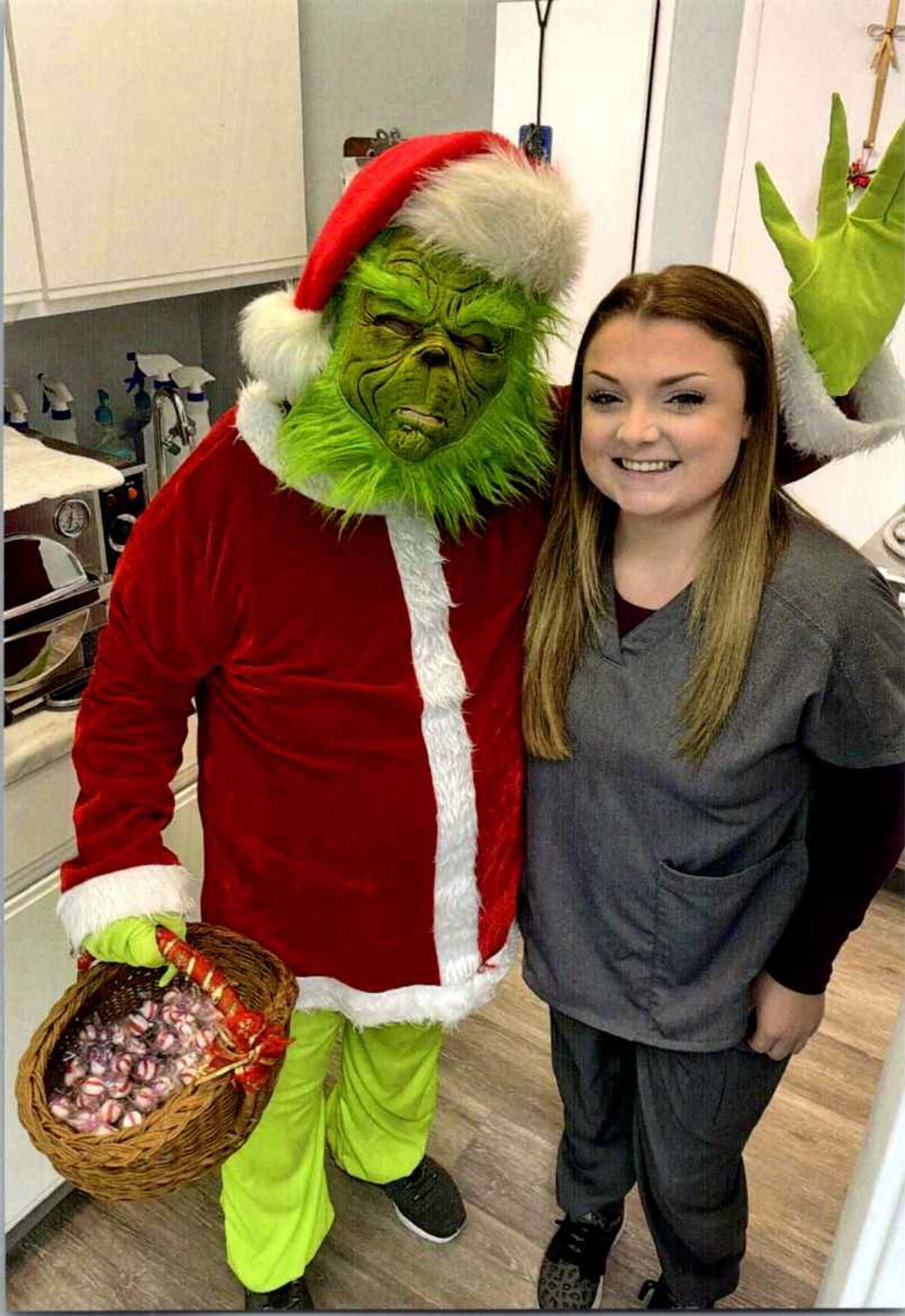 A person in a Santa costume and a woman smiling indoors, holding a basket of wrapped candies.
