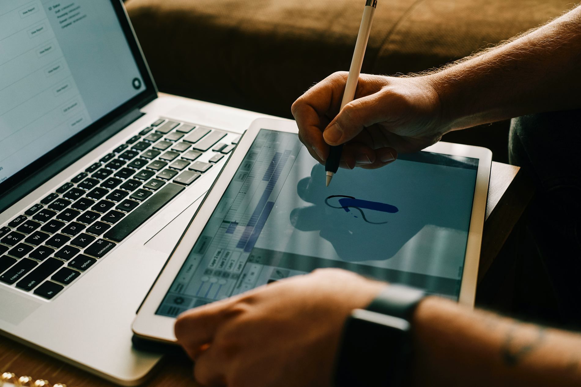 A person is drawing on a tablet in front of a laptop.