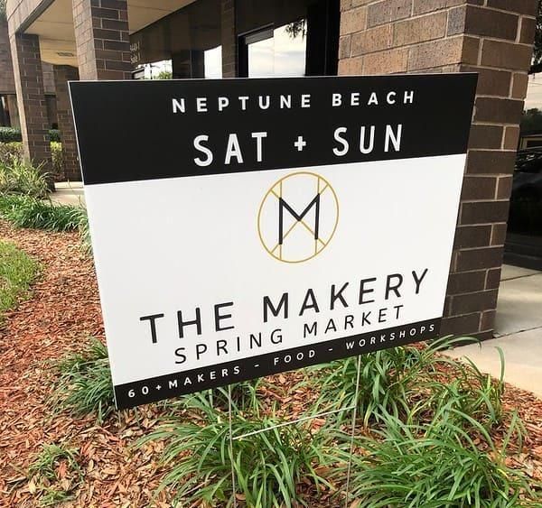 A sign for the makery spring market is sitting in front of a brick building.