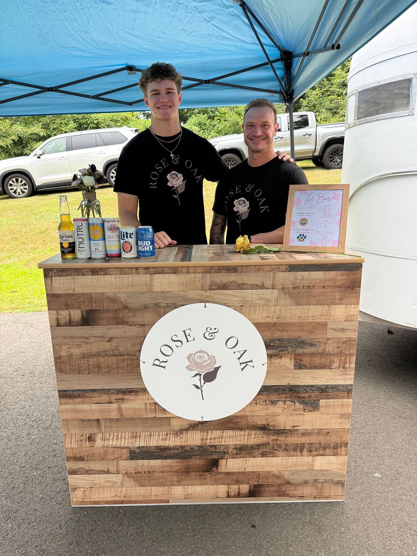 Two people stand behind a wooden booth. 