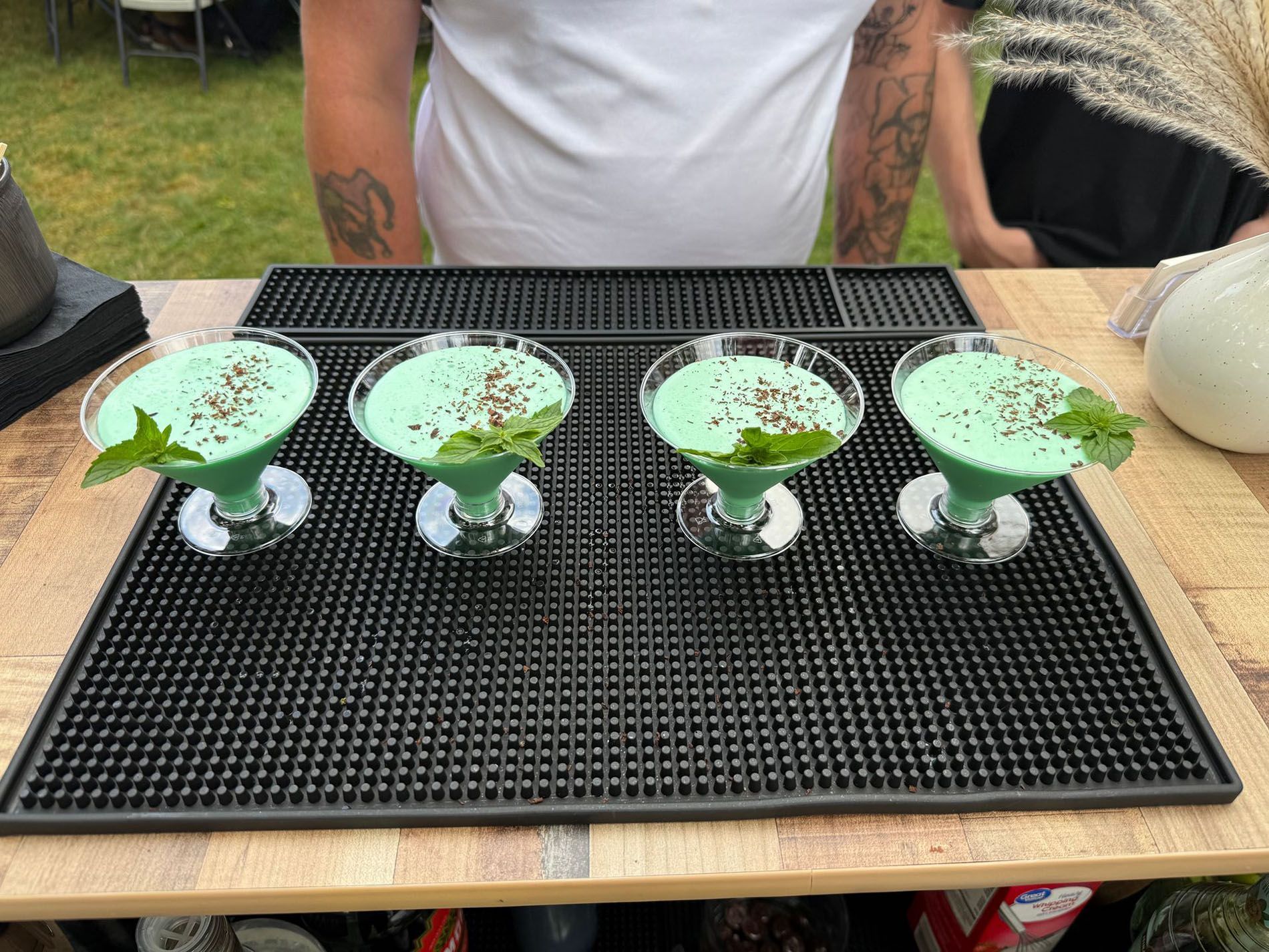 Four green cocktails garnished with mint on a bar. A person stands behind the cocktails.