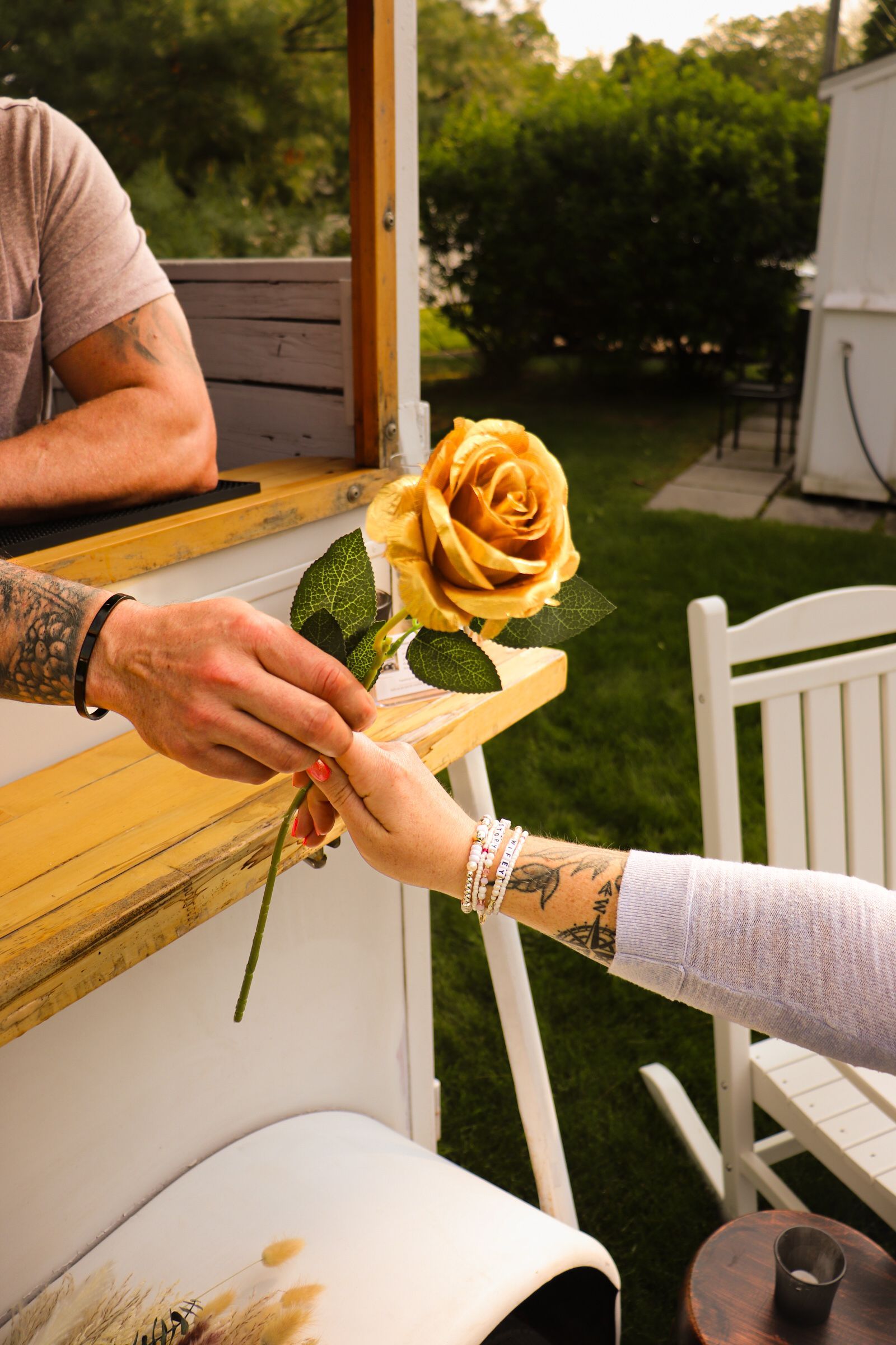 Man offering a golden rose to a woman. The setting is outdoors with a white structure and greenery.