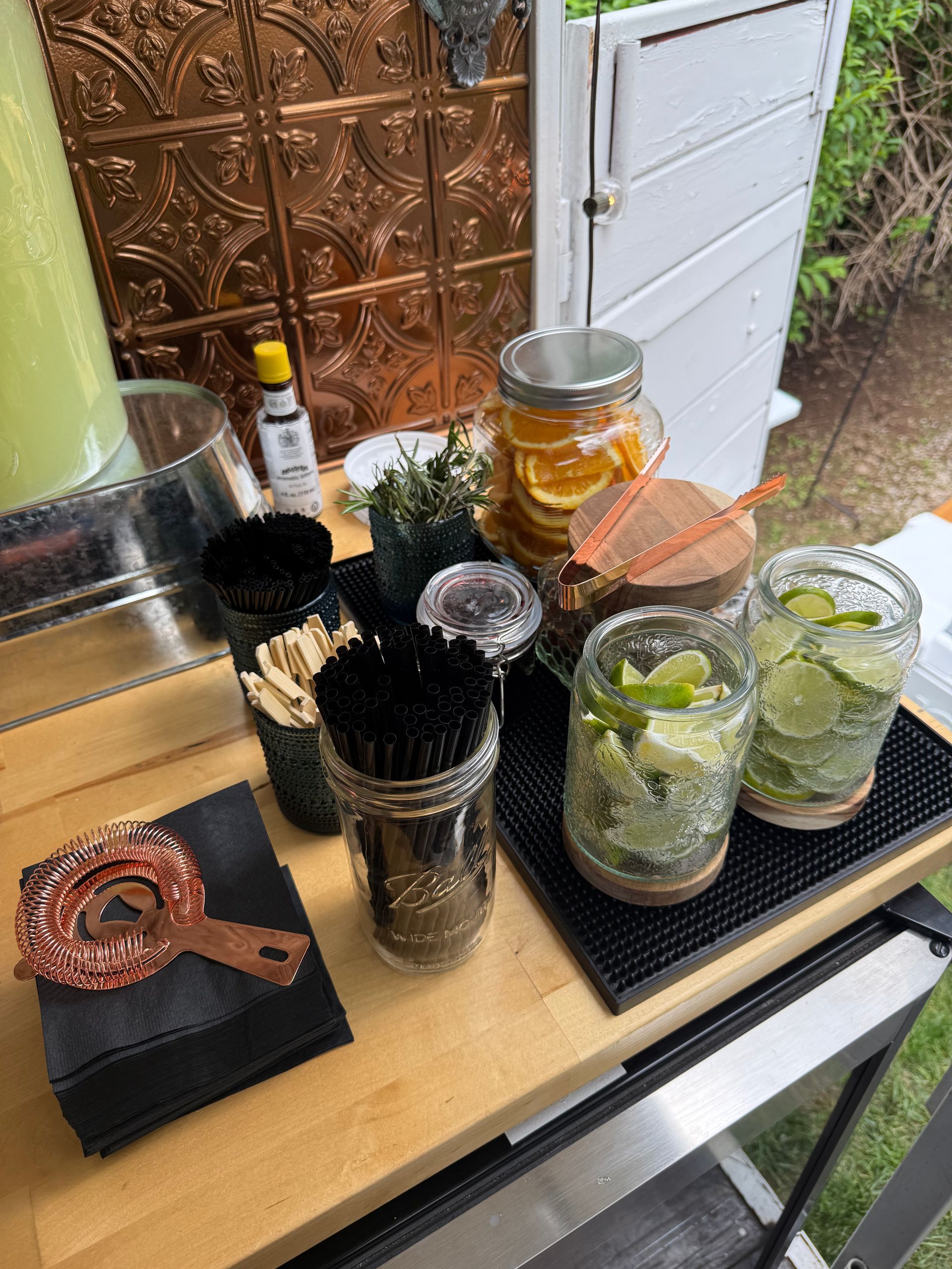 A wooden table topped with glasses , jars , straws , and other items.