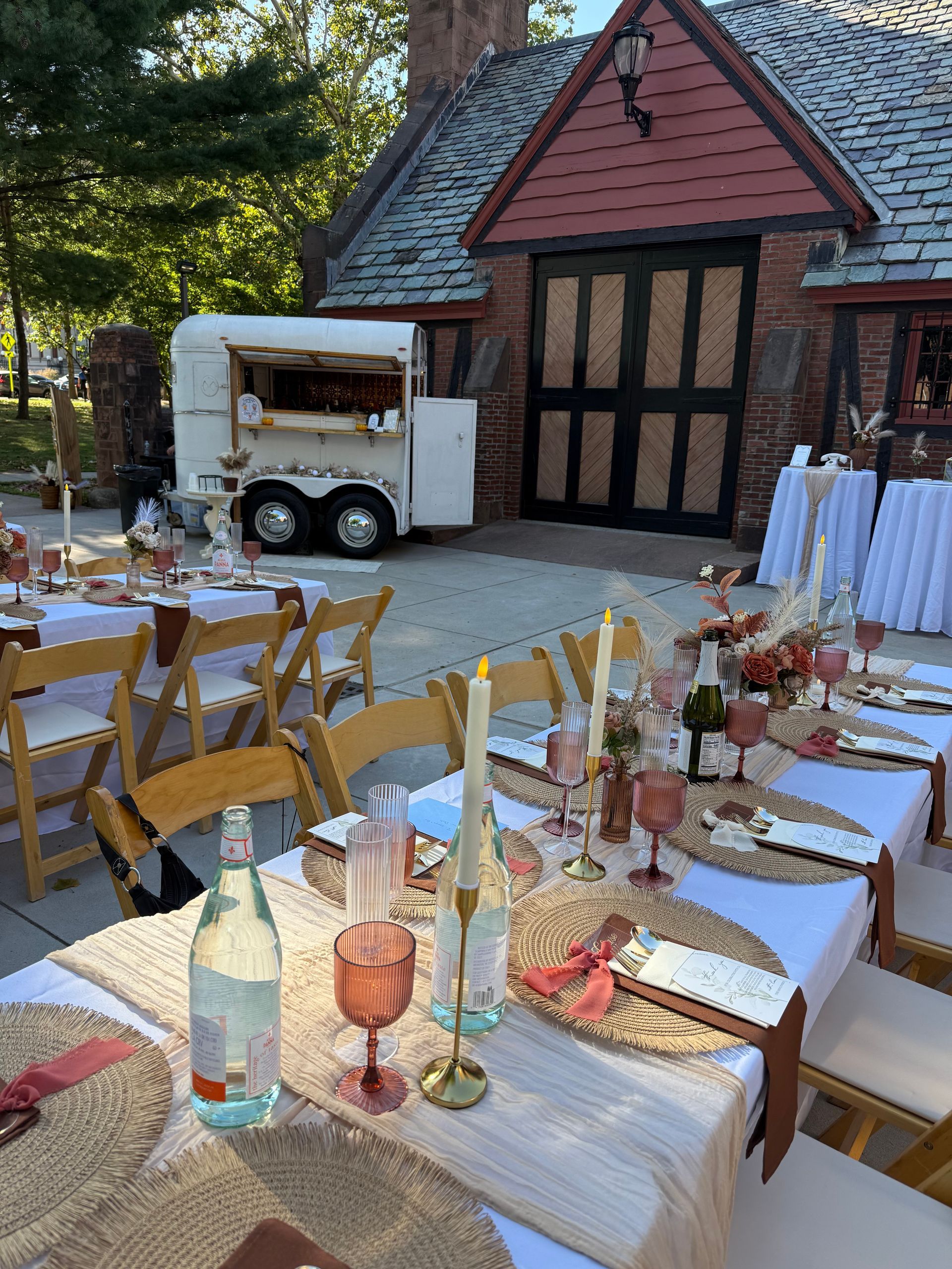 Outdoor event setting with decorated tables, chairs, and a bar in a horse trailer.