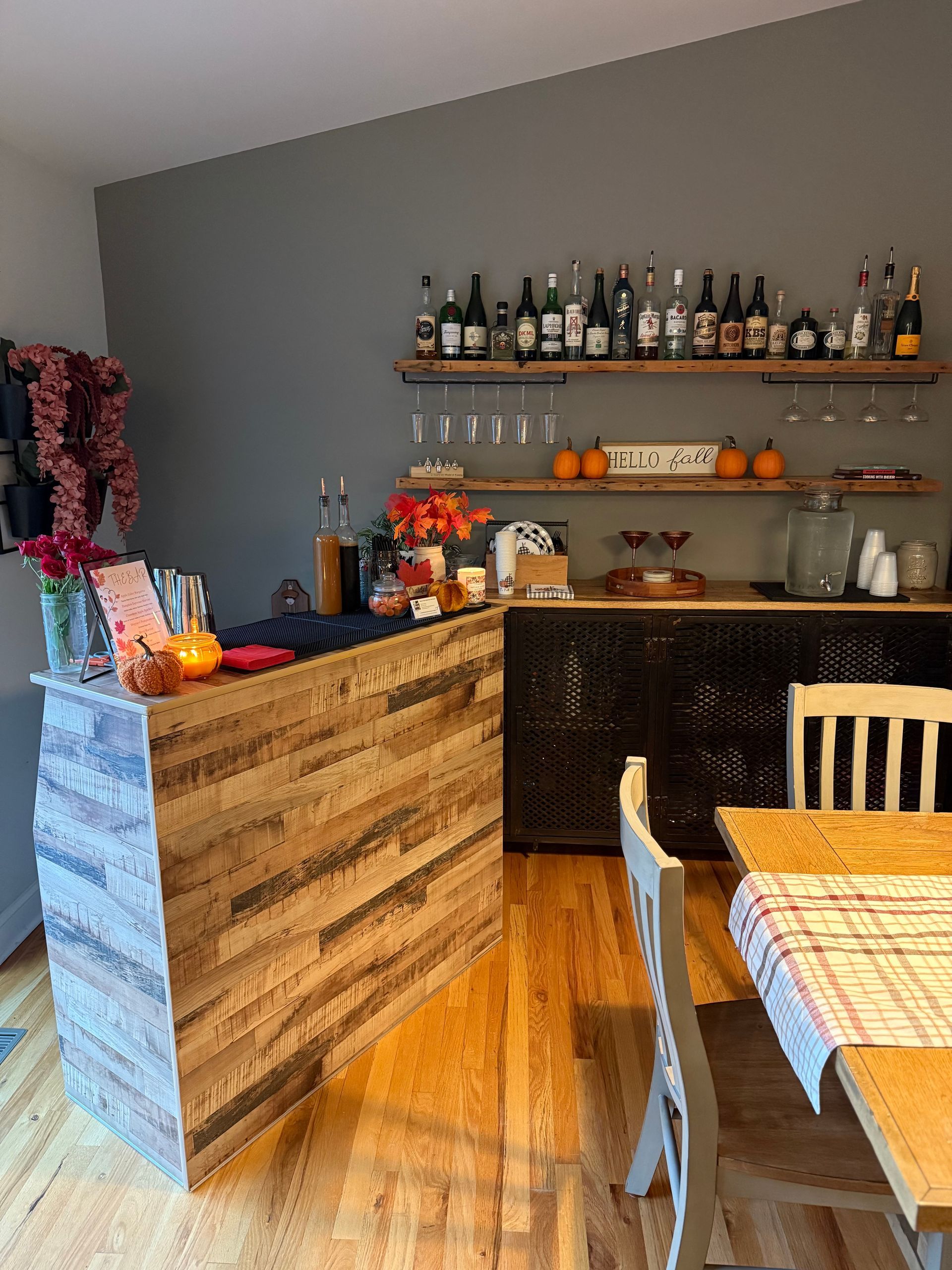 Rustic home bar with wood paneling, shelves of bottles, and fall decor.